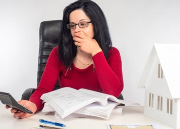 A woman in glasses sitting at a desk with a house model and papers spread out in front of her - Legacy Law Centers