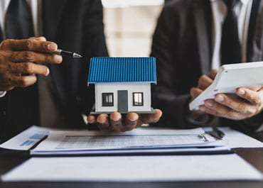 Two persons holding a house model on a desk, discussing an estate plan - Legacy Law Centers