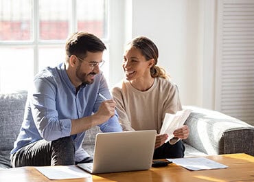 A couple sitting on a couch, focused on a laptop, planning for their future as unmarried partners. - Legacy Law Centers