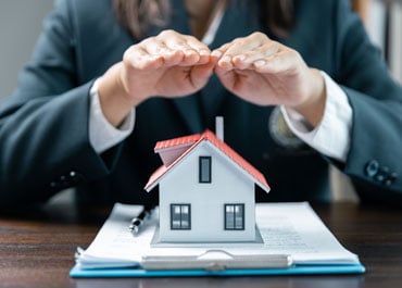 Woman in a suit, her hand on house model, symbolizing Estate Protection - Legacy Law Centers