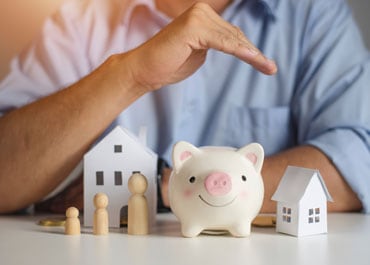 Man holding piggy bank with house and house model, planning for future savings - Legacy Law Centers