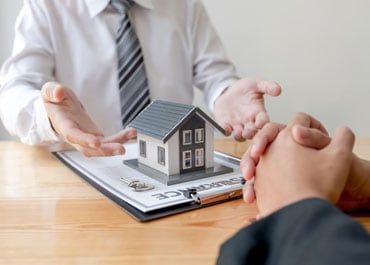 Two individuals holding hands, gazing at a house model, symbolizing estate planning - Legacy Law Centers